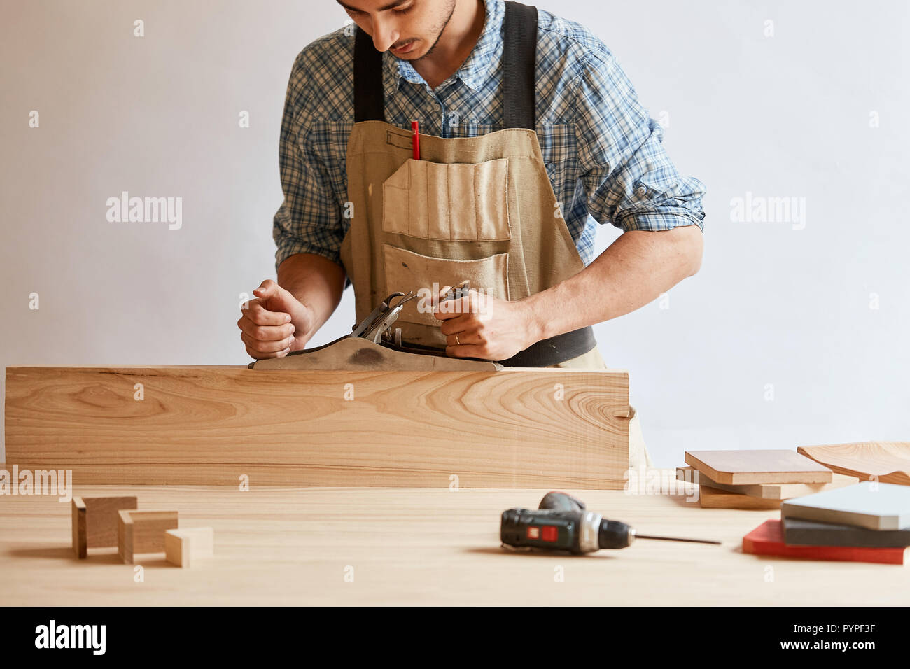 carpenter working with wood using plane against white wall in studio. Stock Photo