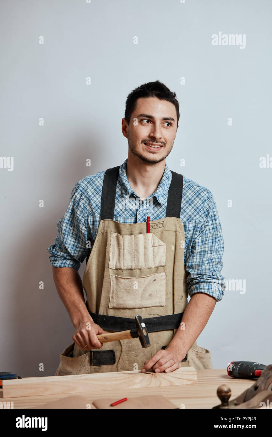 The carpenter hammering down a nail to wooden plank, making a furniture