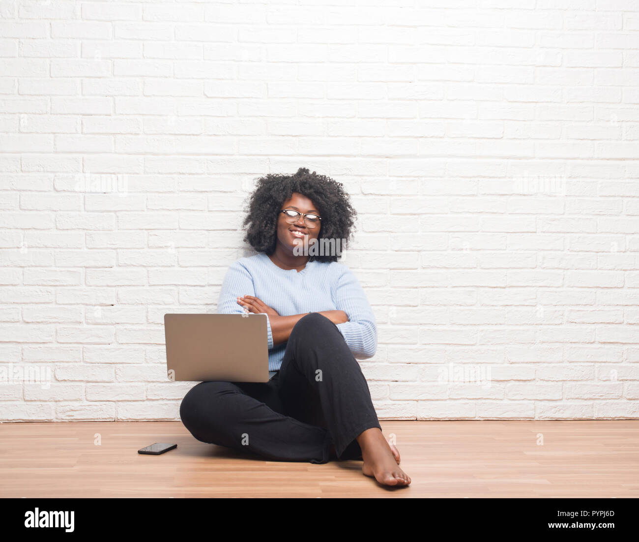 Young african american woman sitting on the floor using laptop at home ...