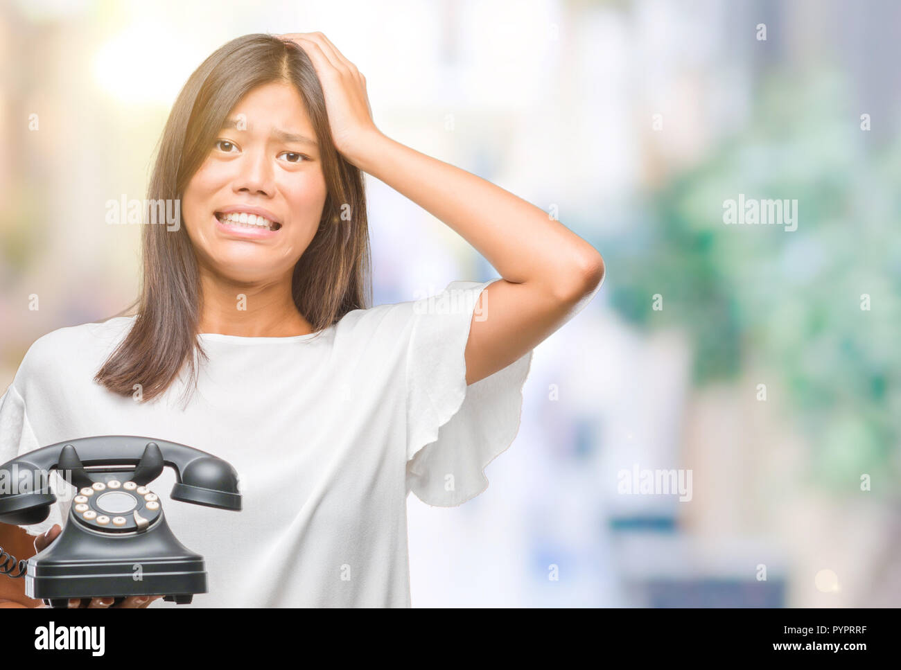 Young asian woman holding vintagera telephone over isolated background stressed with hand on head, shocked with shame and surprise face, angry and fru Stock Photo
