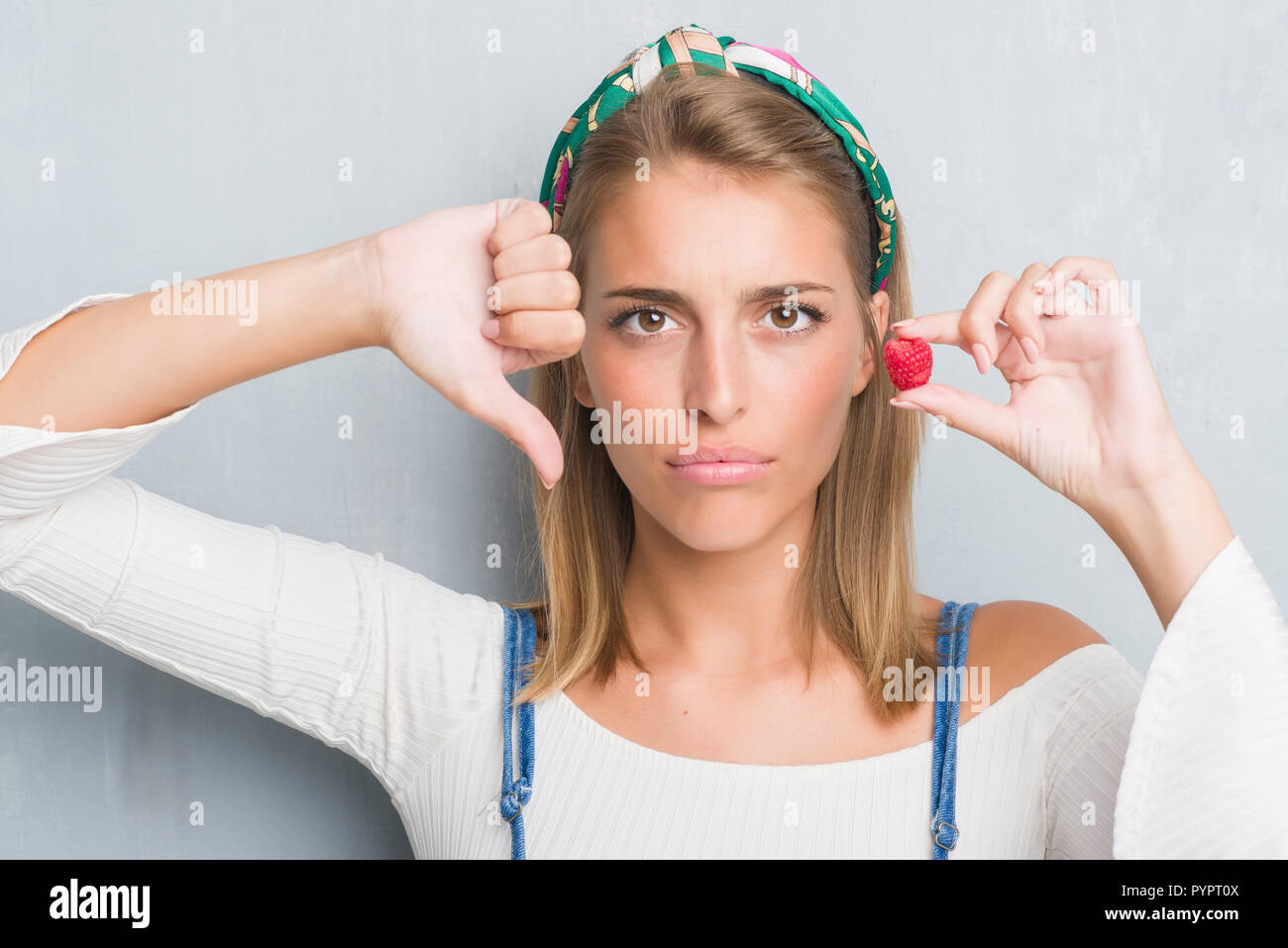 Beautiful young woman over grunge grey wall eating fresh raspberry with ...