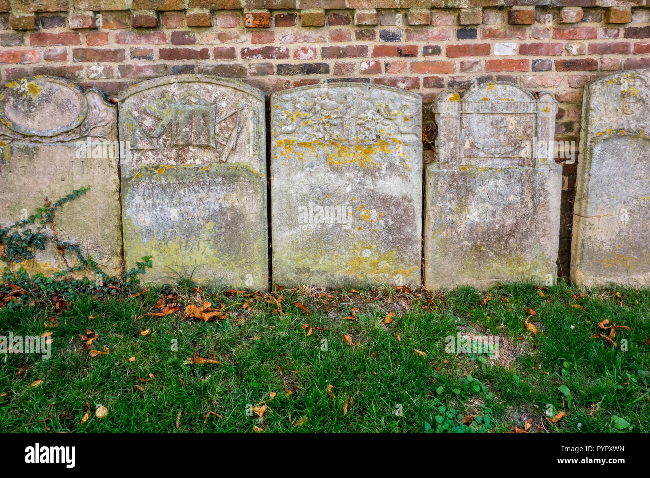 Grave stones lined up against a brick wall St Mary the Virgin parish church Saffron Walden, historic market town in Uttlesford, Essex, UK Stock Photo