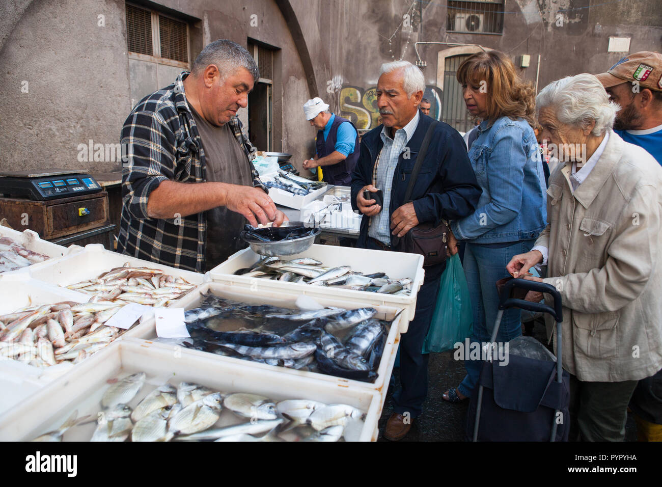 A fishmonger serves customers in the fish market in Catania, Sicily Stock Photo