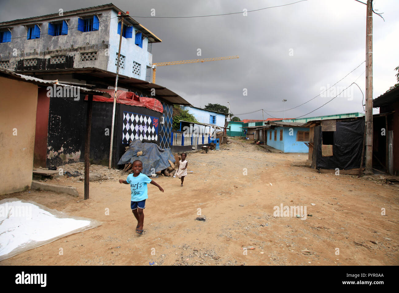 Boy and girl run down a dirt street before a rain storm in Blockhauss, Abidjan, Cote D'Ivoire Stock Photo
