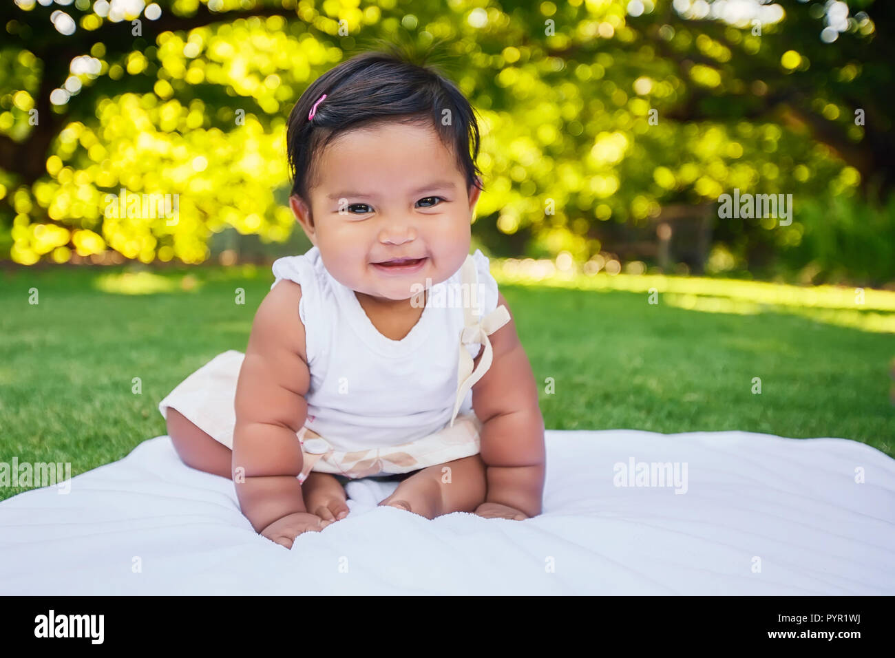 Adorable little baby girl with cute smile sitting unsupported and starting to take first crawling steps, being independent and of Mexican heritage Stock Photo