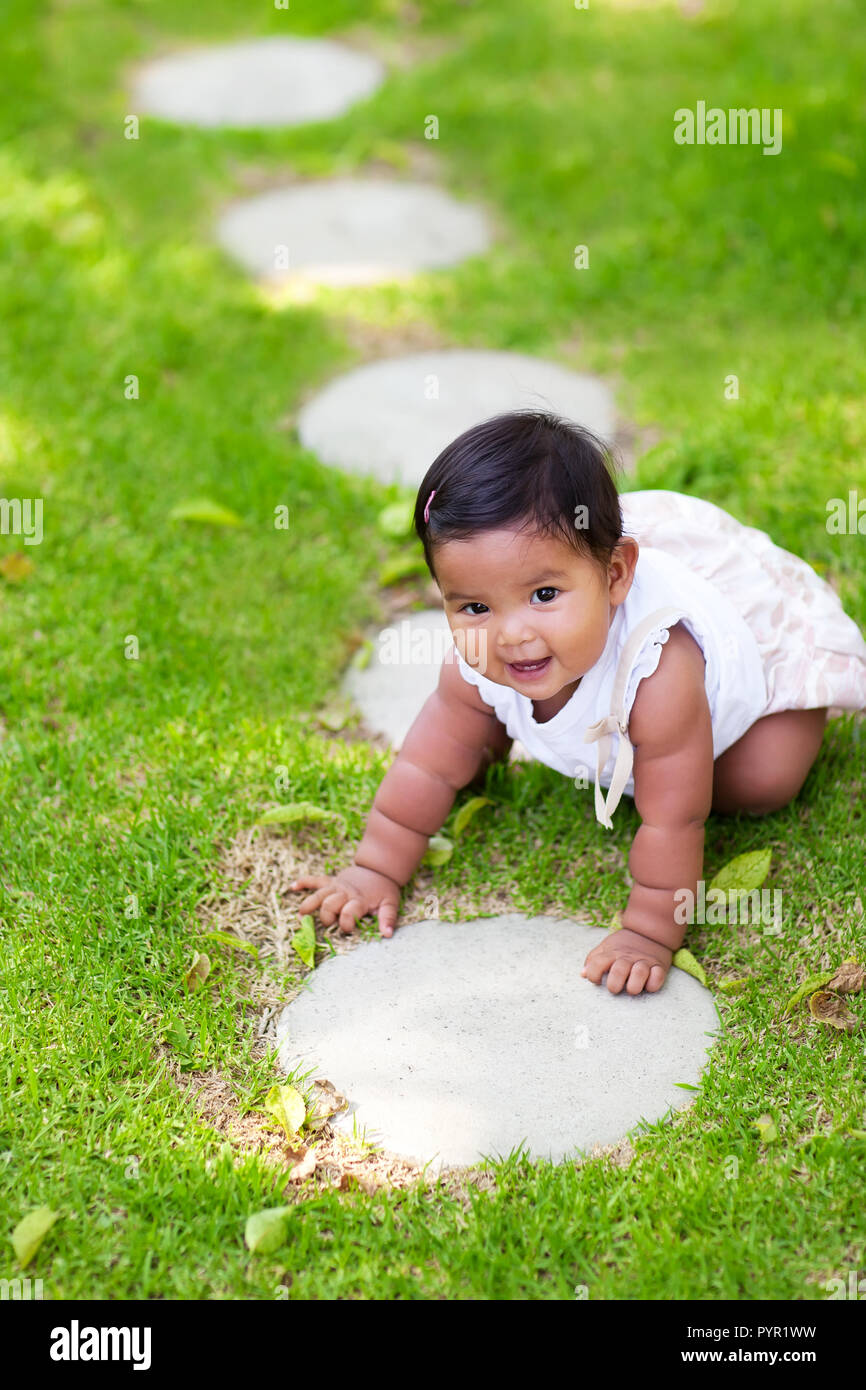 Latino baby girl beginning or learning to crawl on a green lawn with many steps to walk on. The baby girl is crawling and looks happy. Stock Photo