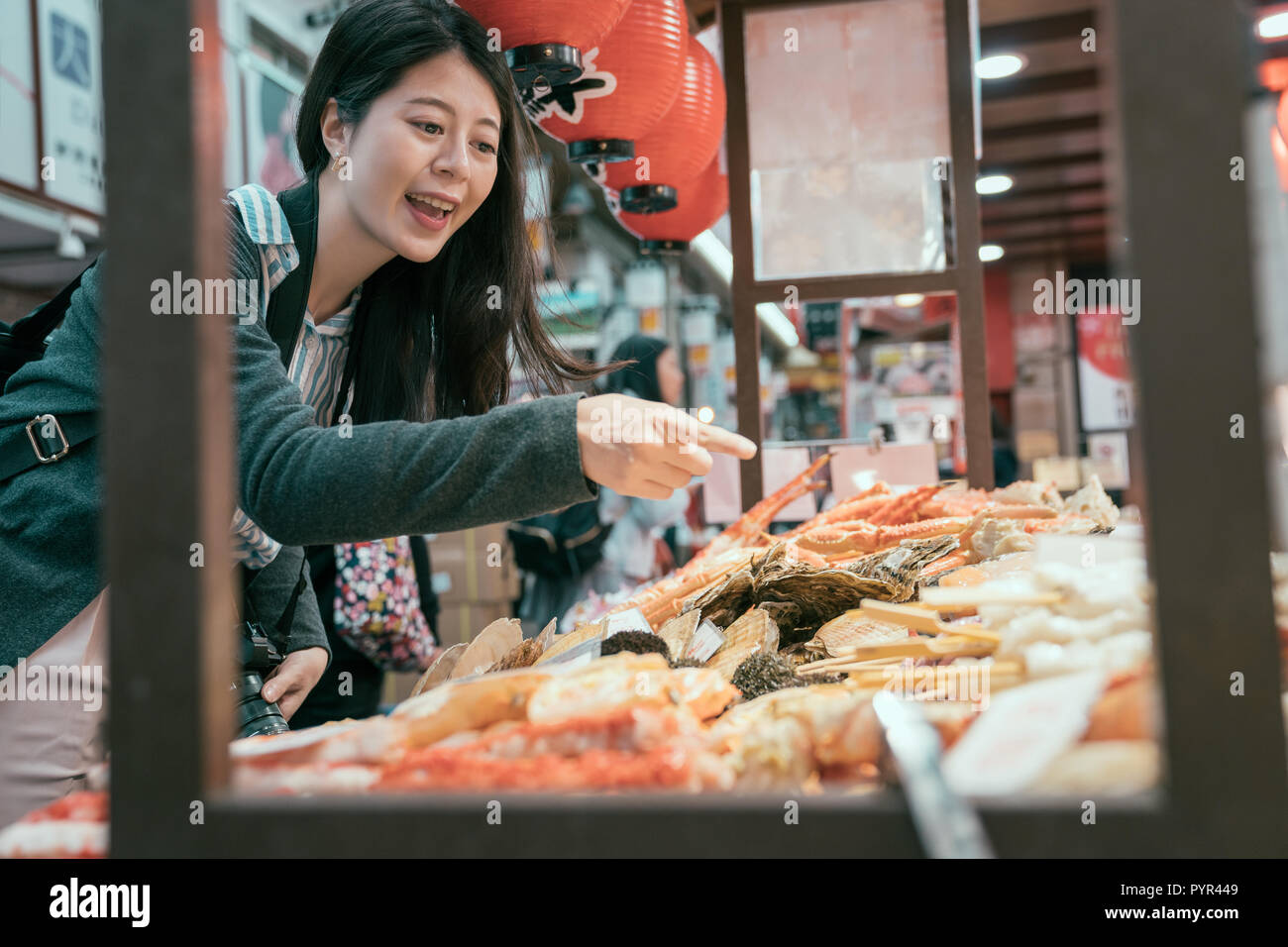 Japan travel lady pointing at the seafood on the mobile kitchen. girl tourist experience japanese culture. young traveler hungrily buying street food. Stock Photo