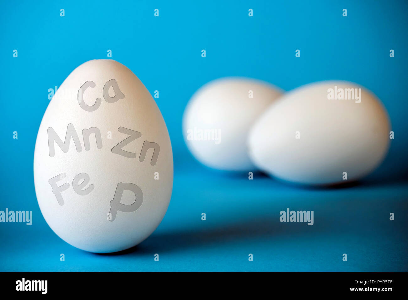 Chicken egg contains many microelements of calcium, phosphorus, manganese, iron, zinc, Eggs in a shell with a symbol Ca, P, Zn, Mn, Fe on a blue backg Stock Photo