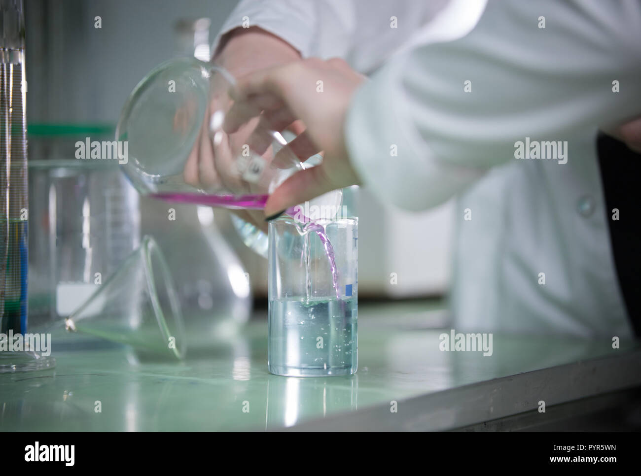Table full of flasks. Chemical lab. Hands pouring liquid Stock Photo
