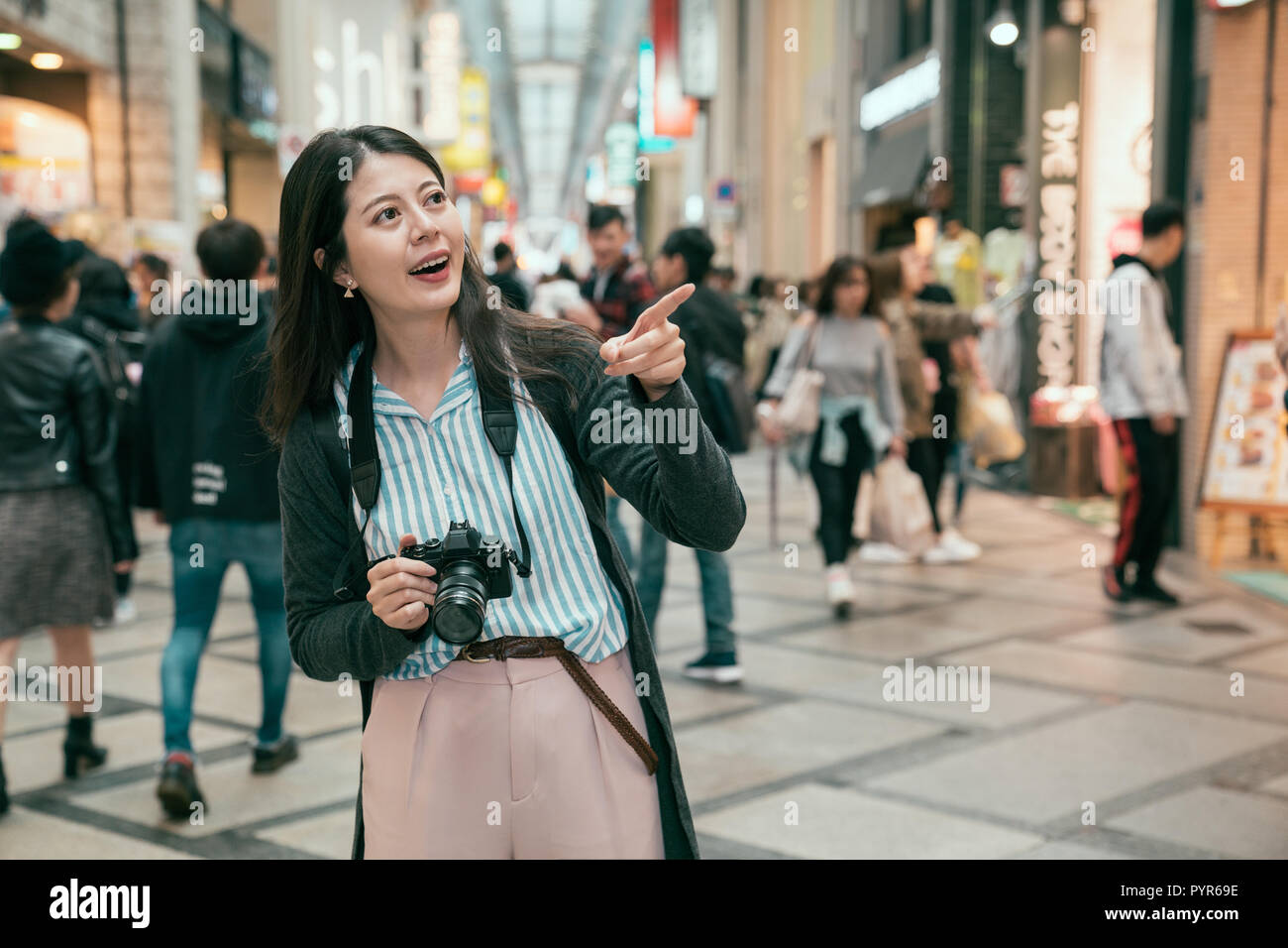 young asian tourist stand in the street in osaka. lady joyfully pointing to the shop in shinsaibashi. japanese holiday shopping lifestyle. Stock Photo