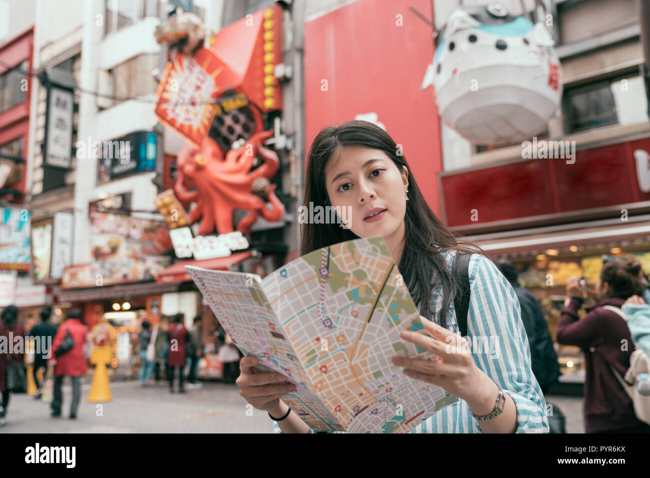 young lady traveler holding map on the dotonbori. cute tourist finding right direction on the teeming street in osaka. female traveler trip in japan a Stock Photo