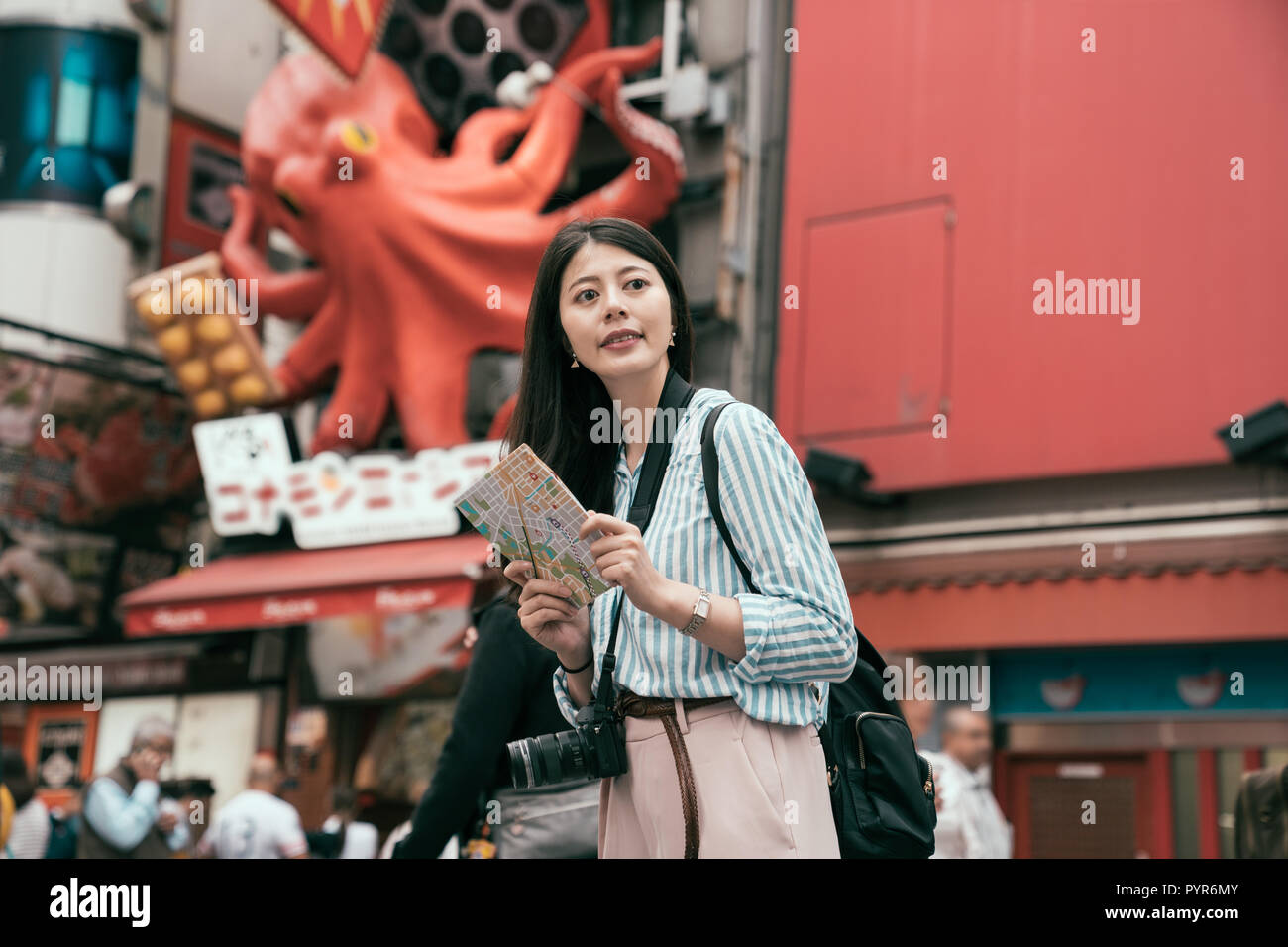 lady traveler holding map standing on the busy street on the dotonbori. female lady photographer travel in osaka. happy female tourist searching road  Stock Photo