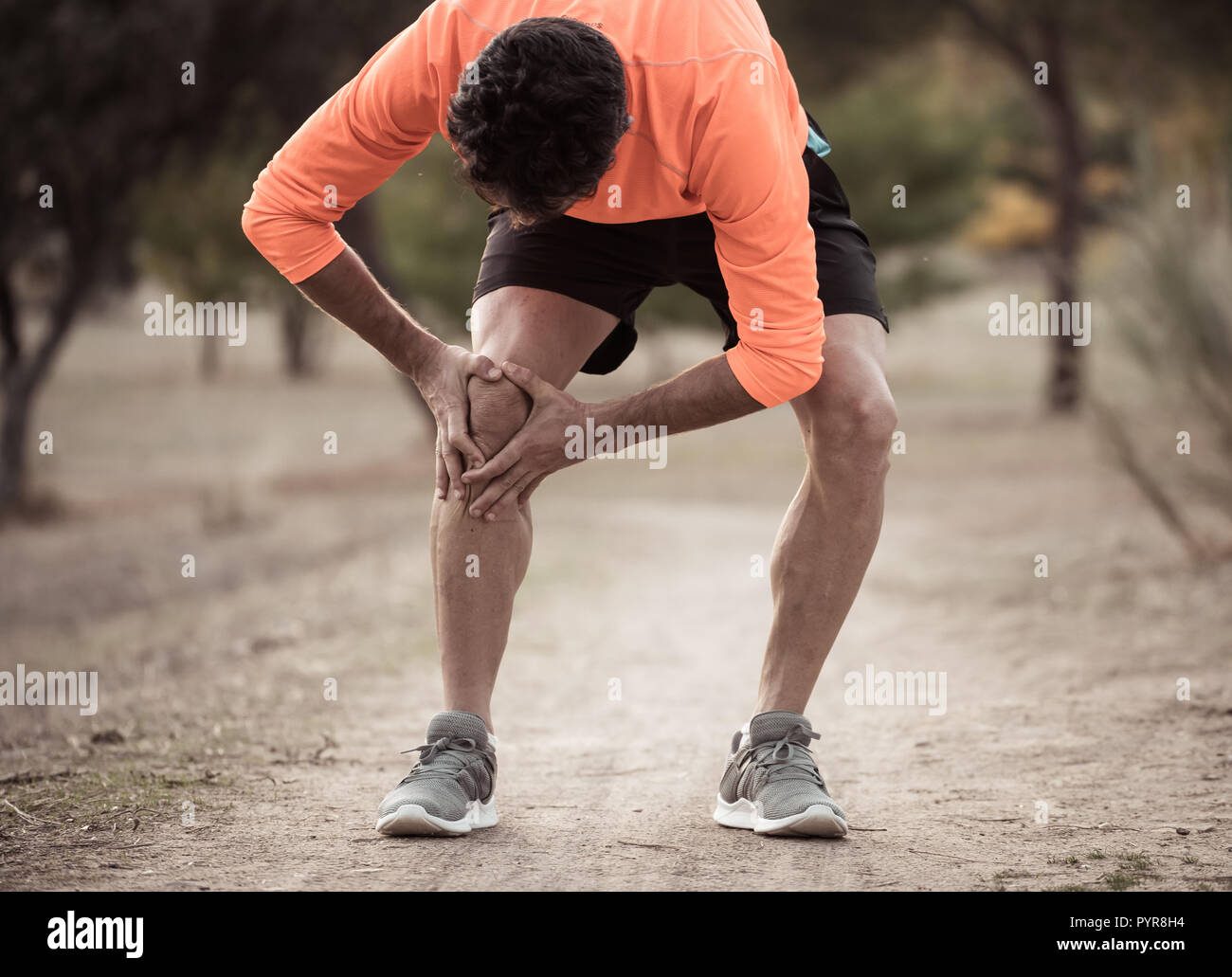 Young fit man holding knee with his hands in pain after suffering