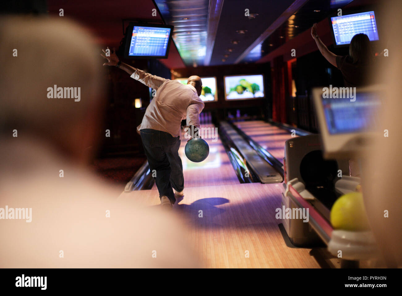 Mid adult man bowling a ball at a bowling alley watched on by friends Stock Photo Alamy