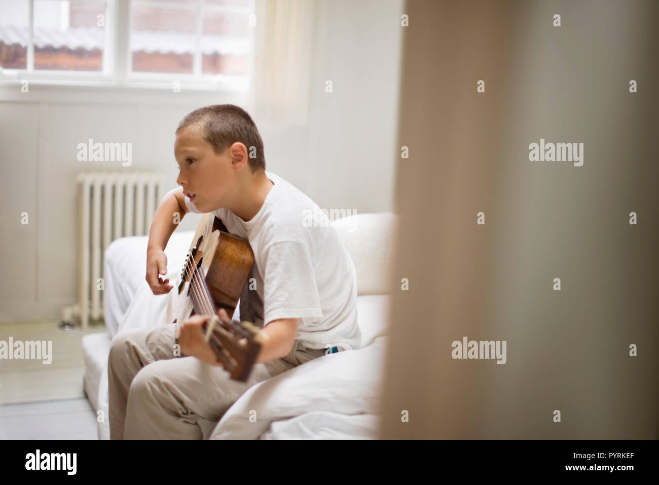 Boy playing an acoustic guitar in a bedroom. Stock Photo