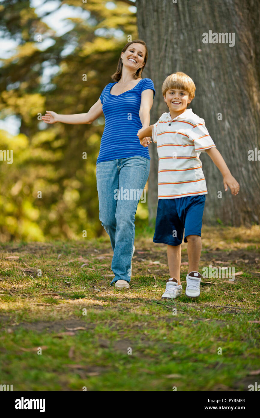Happy young boy pulling his mother by the hand in a park. Stock Photo