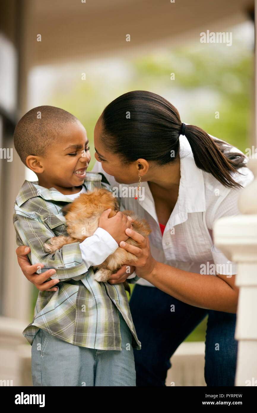 Happy young boy holding a puppy in his arms next to his mother. Stock Photo