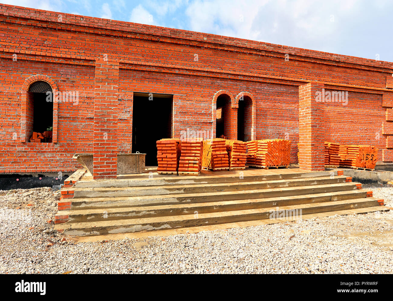 Red bricks on pallets near the wall of the building under construction Stock Photo