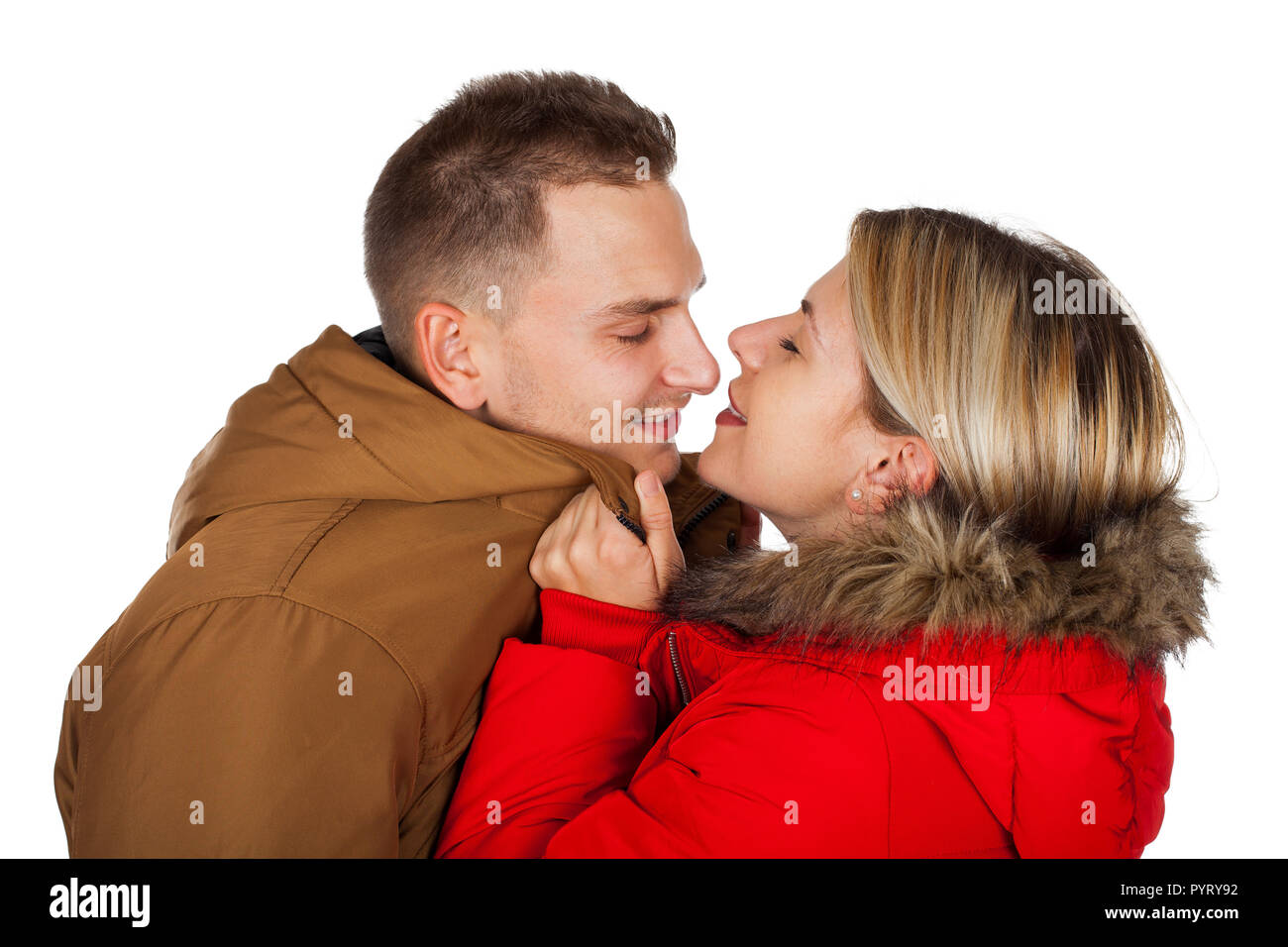 Couple wearing winter clothing - red and brown hooded parka jackets -  kissing on isolated background Stock Photo - Alamy