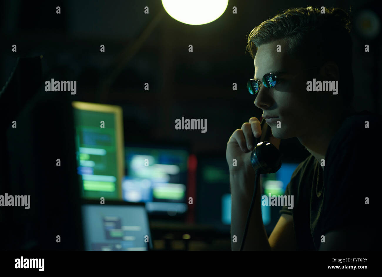 Hacker with sunglasses holding a telephone receiver and computer screens, coding and system hacking concept Stock Photo