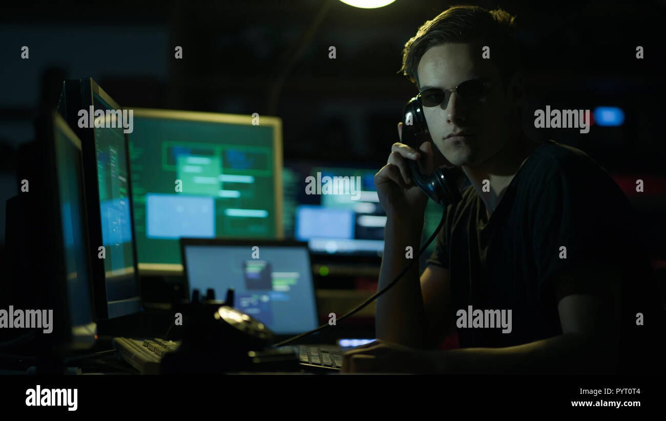 Hacker with sunglasses holding a telephone receiver and computer screens, coding and system hacking concept Stock Photo