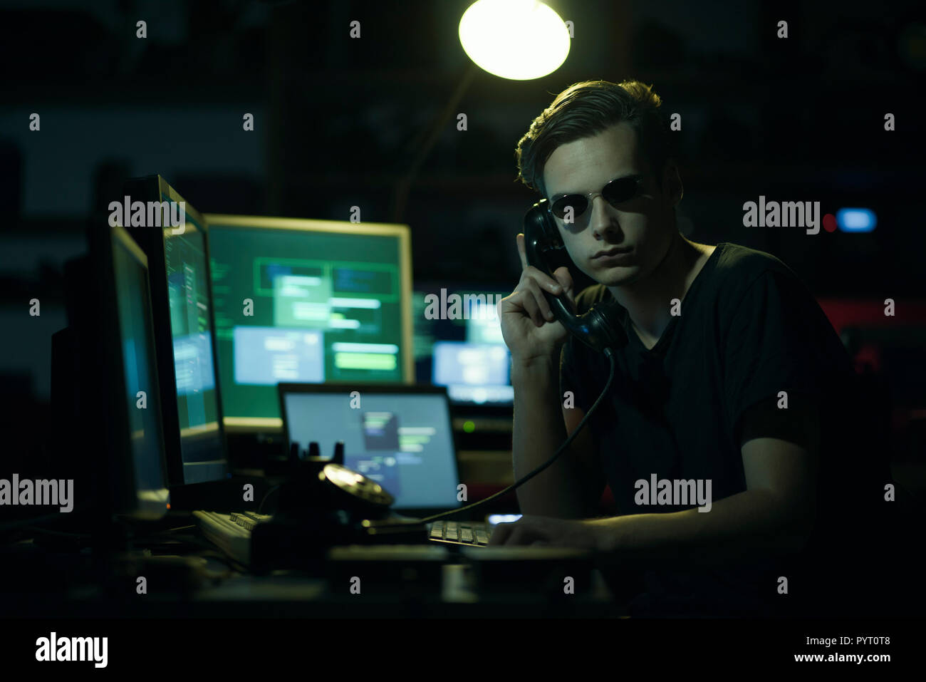Hacker with sunglasses holding a telephone receiver and computer screens, coding and system hacking concept Stock Photo