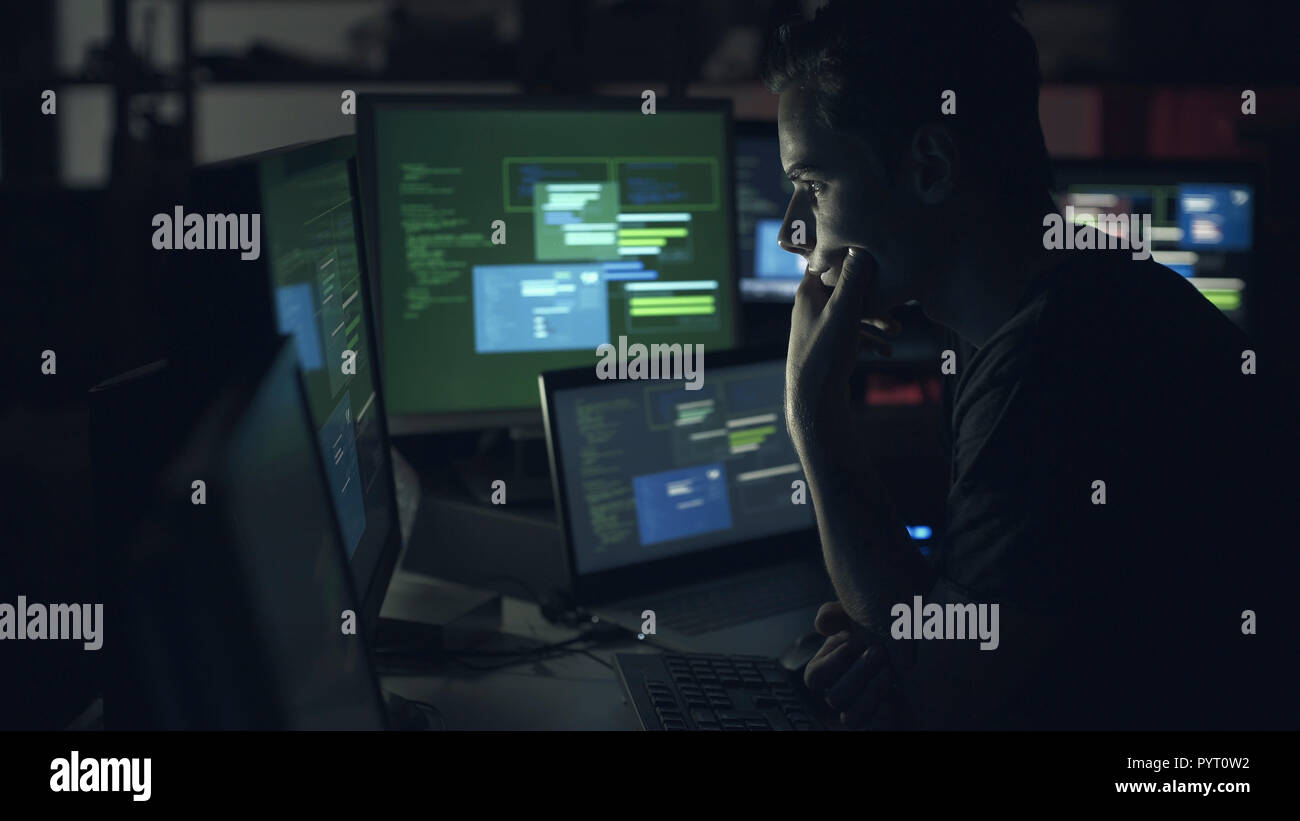 Young computer developer working with computers late at night, coding