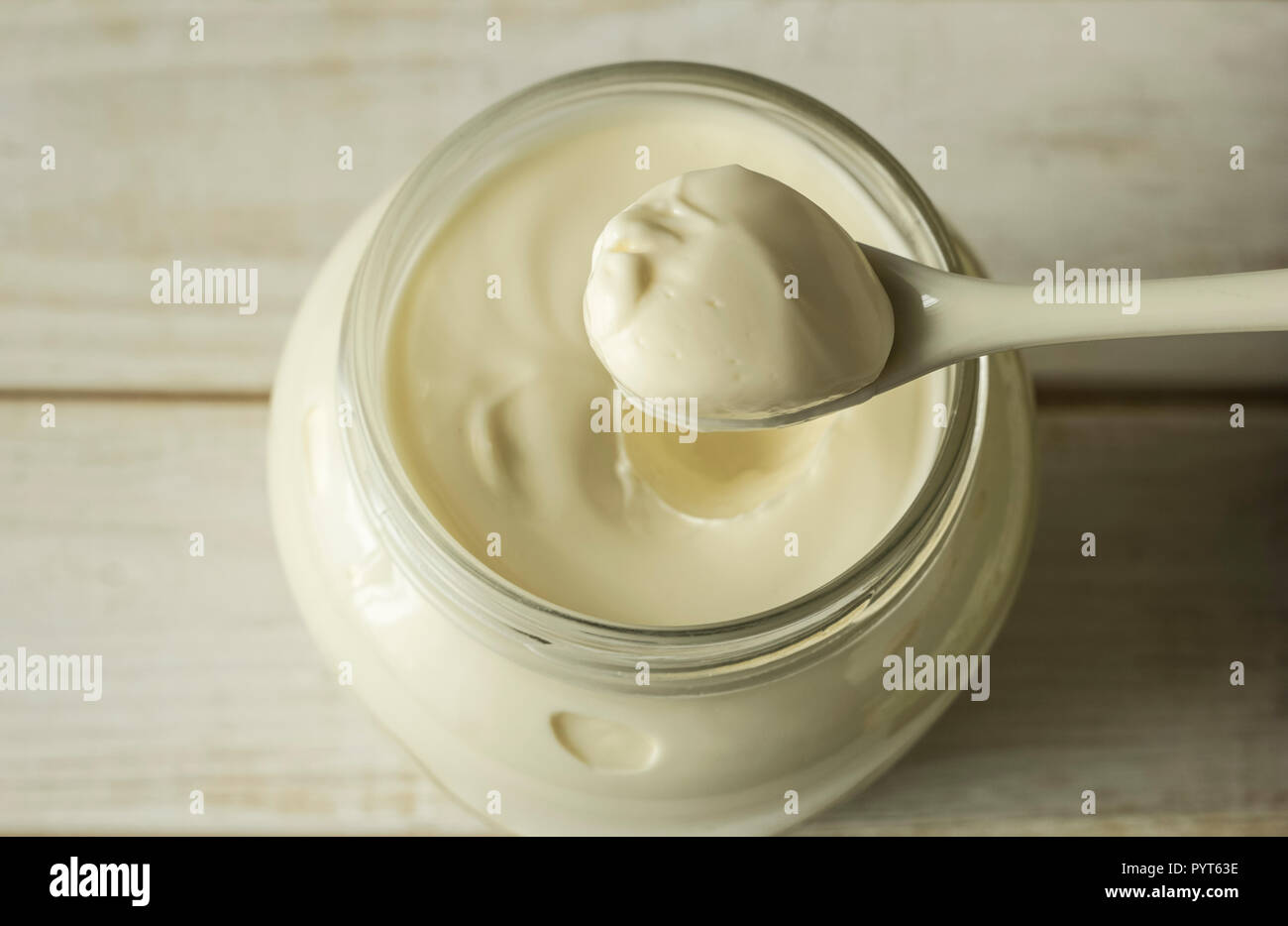 Mayonnaise in a glass jar with a spoon on white wooden boards. Stock Photo