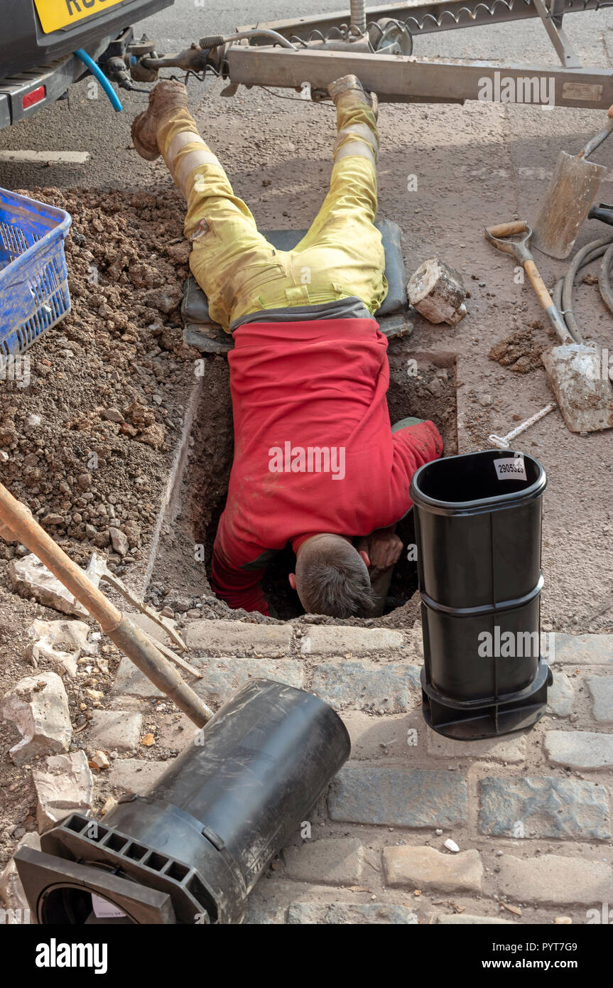 Installing a new water meter in the road. UK. Man leaning into a hole to make the installation Stock Photo