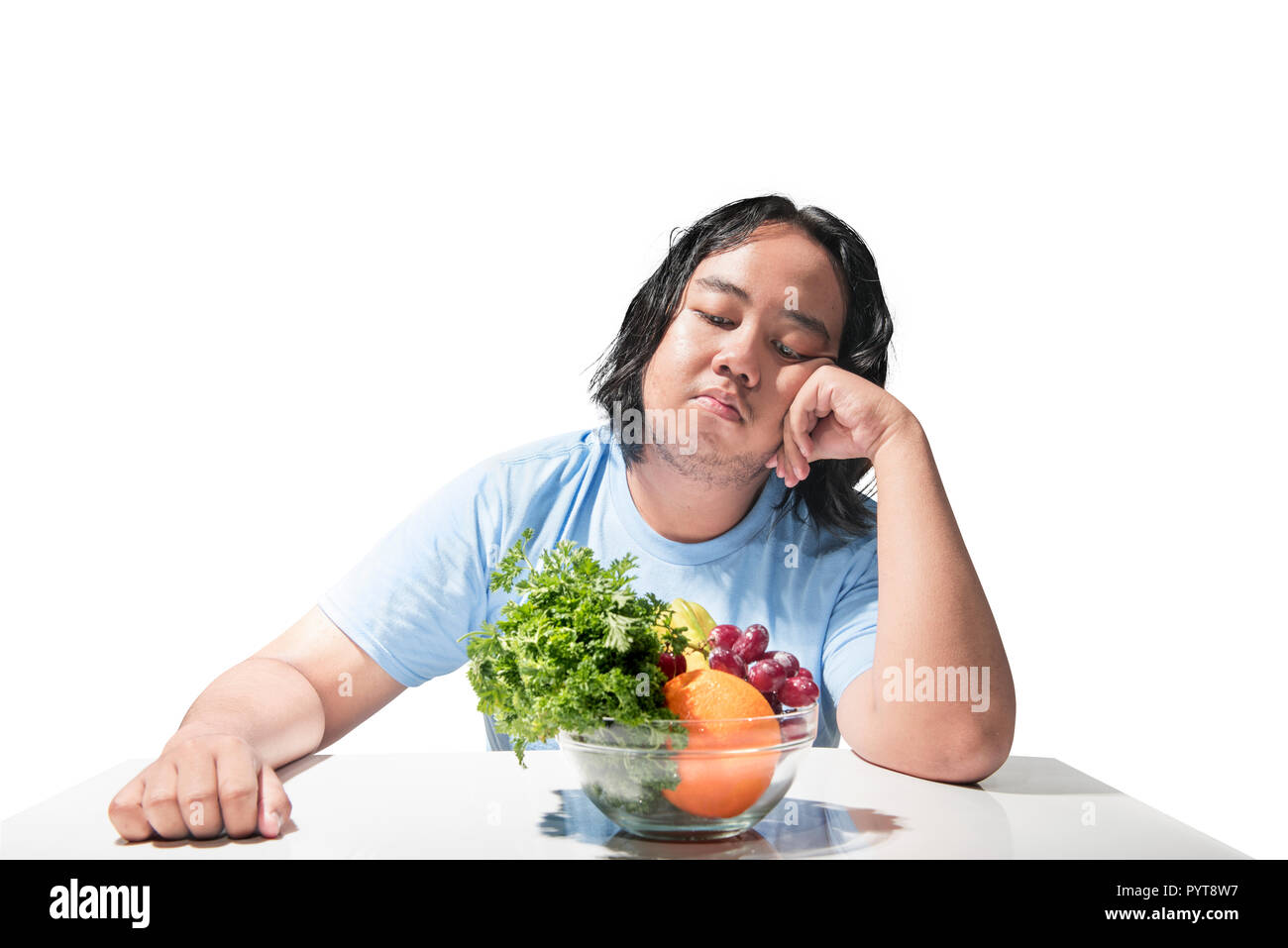 Asian fat man sad looking at healthy food (fruit and vegetables) on the desk isolated over white background. Fat man diet concept Stock Photo