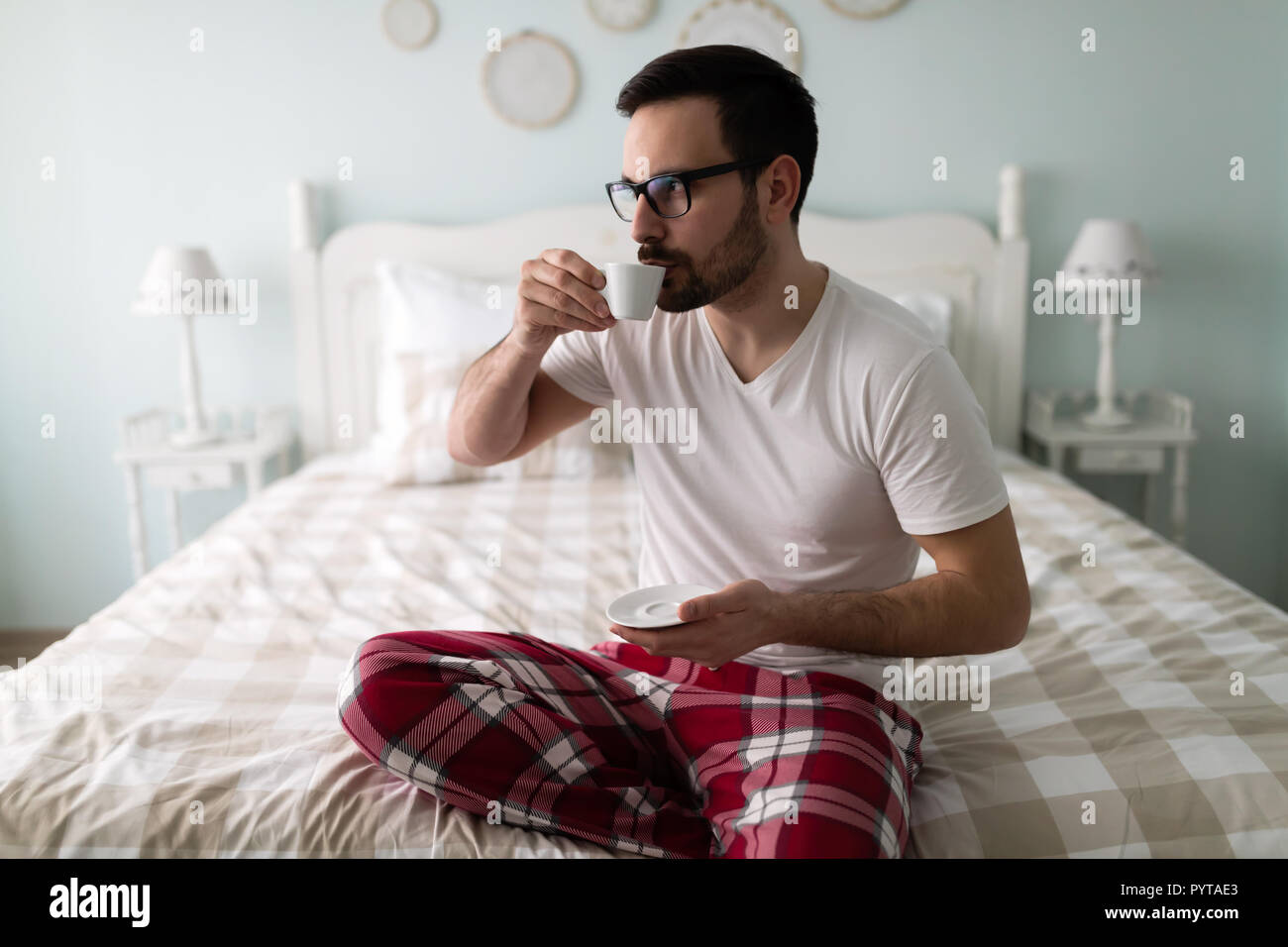 Young handsome man drinking coffee on his bed Stock Photo