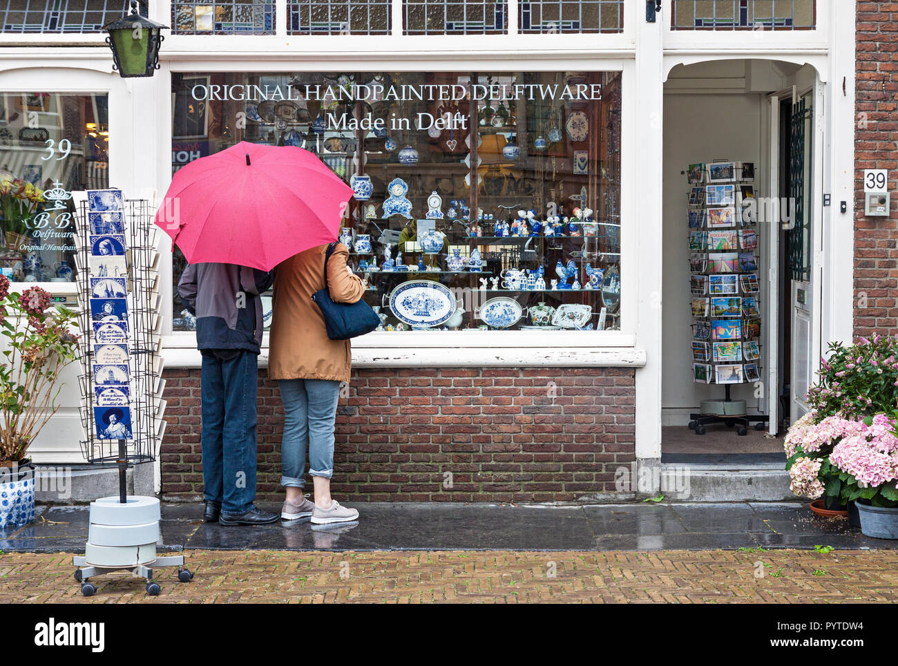 Two tourists with red umbrella looking at window display of traditional Dutch handpainted pottery shop in Delft, Stock Photo