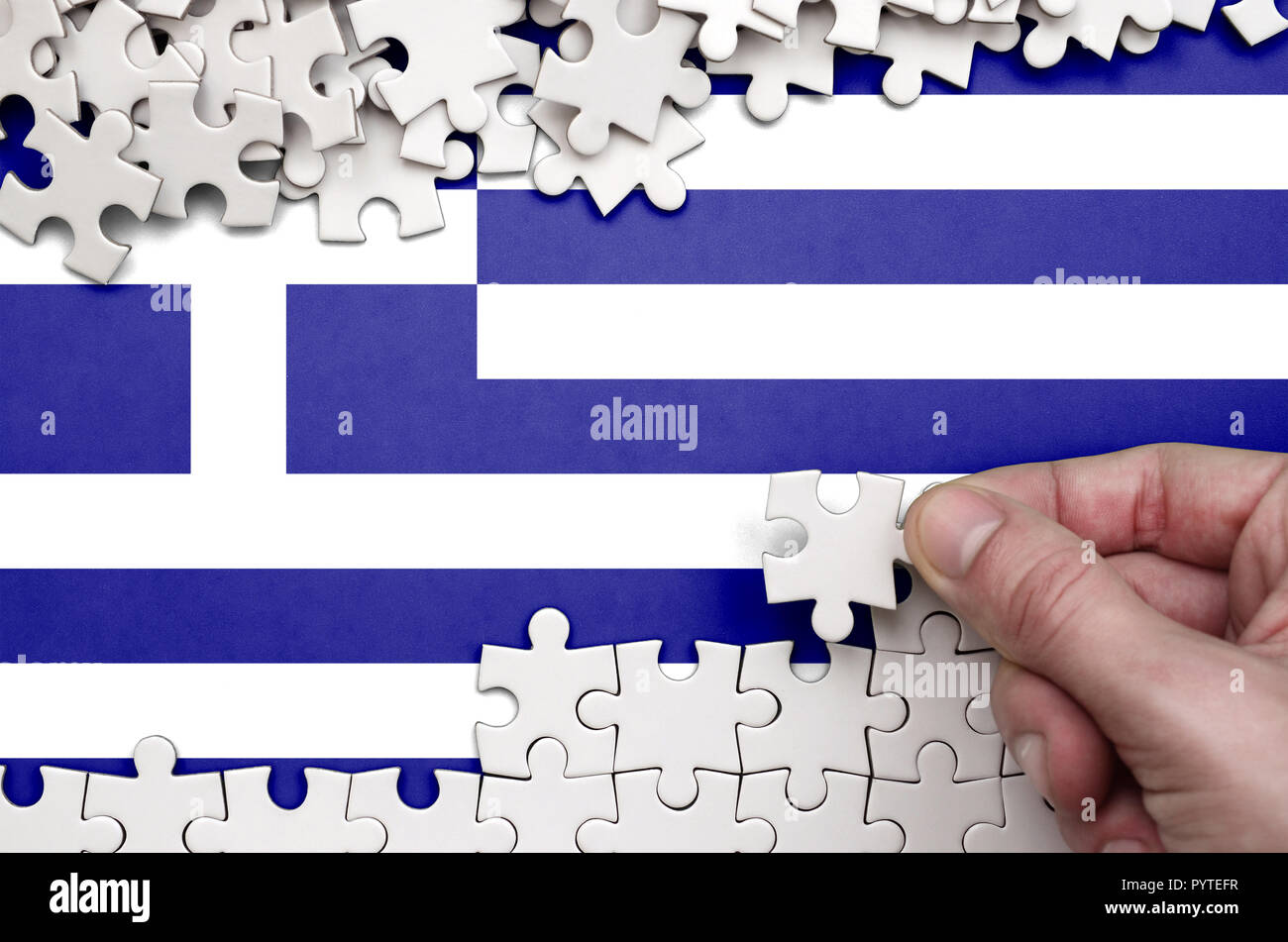 Greece flag is depicted on a table on which the human hand folds a ...