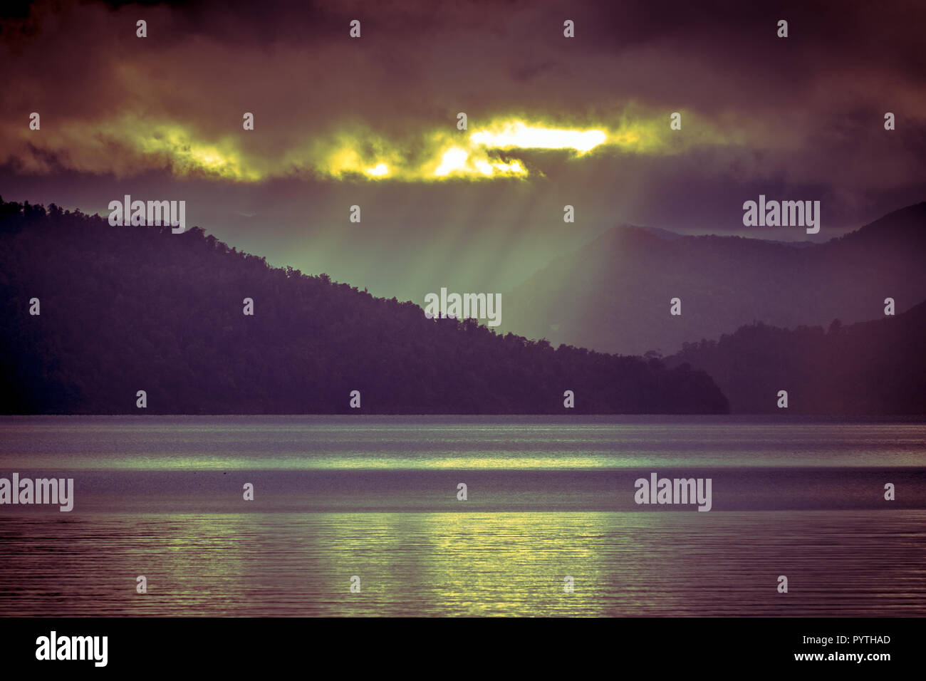 Rays of sun falling through the clouds over pristine mountain lake Wakaremoana in New Zealand in vintage toning Stock Photo