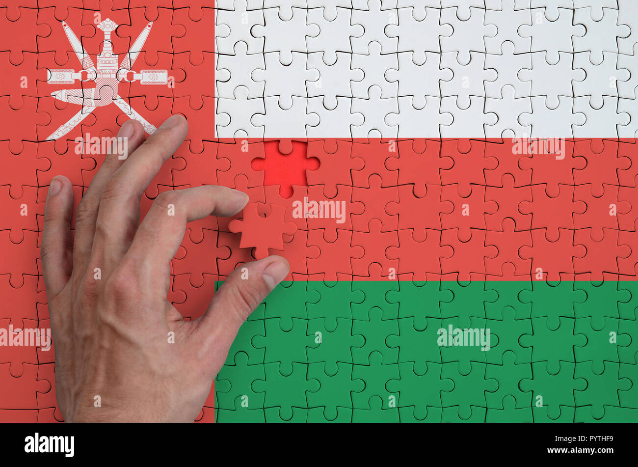 Oman flag  is depicted on a puzzle, which the man's hand completes to fold. Stock Photo