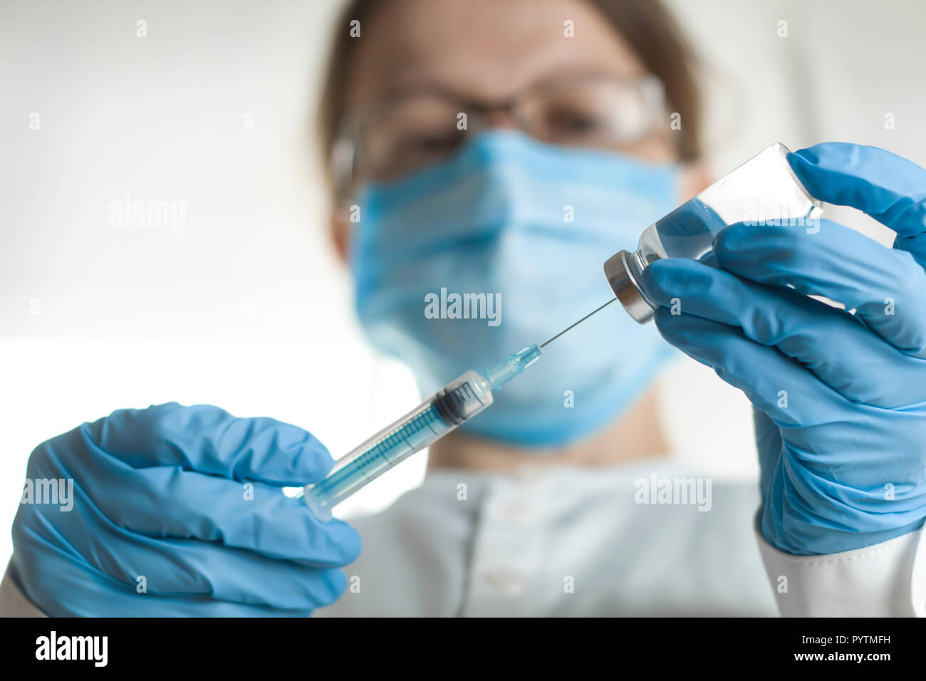A syringe and a bottle with an injection solution, against the background of a medical worker. The doctor is holding a syringe with vaccination. Stock Photo