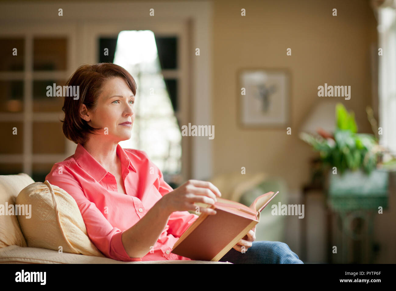 Mid adult woman sitting in a living room reading a book Stock Photo - Alamy