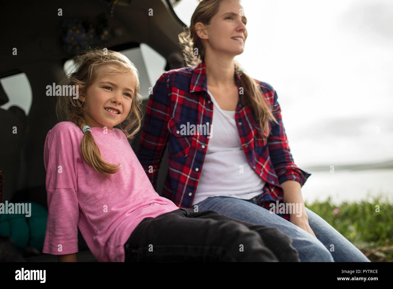 Little girl enjoys sitting in the back of the car with her mother and looking at the countryside view. Stock Photo