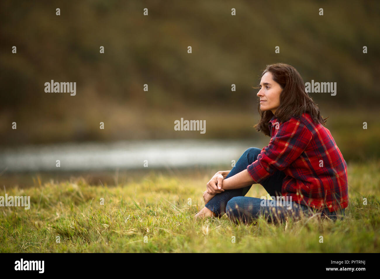 Portrait of a thoughtful mid adult woman sitting in a grassy field. Stock Photo