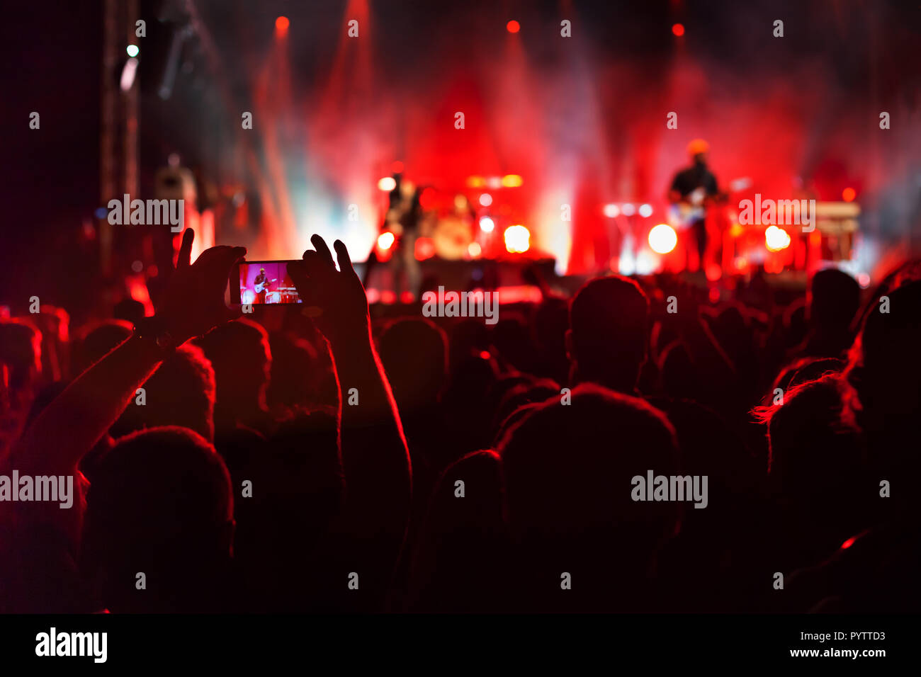 hands filming concert with smartphone, crowd of spectators watching musicians playing music and singing on stage Stock Photo