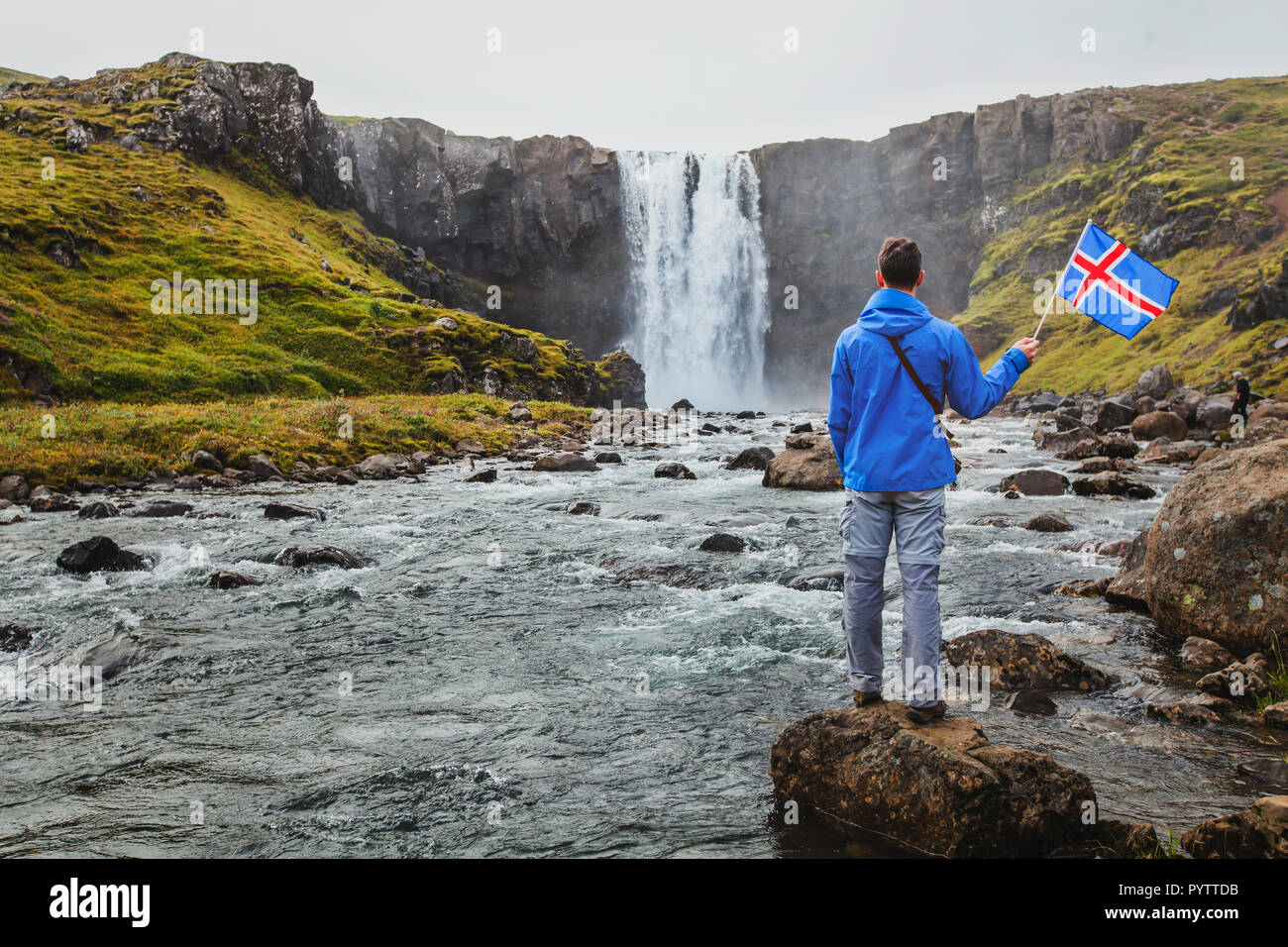 travel to Iceland, tourist holding icelandic flag near scenic waterfall Stock Photo