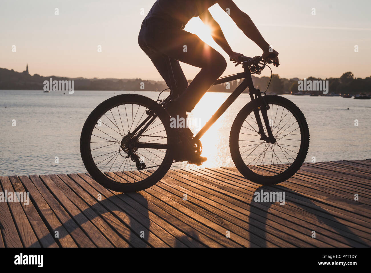 man riding bicycle at sunset, cycling in summer, silhouette of cyclist near the lake Stock Photo