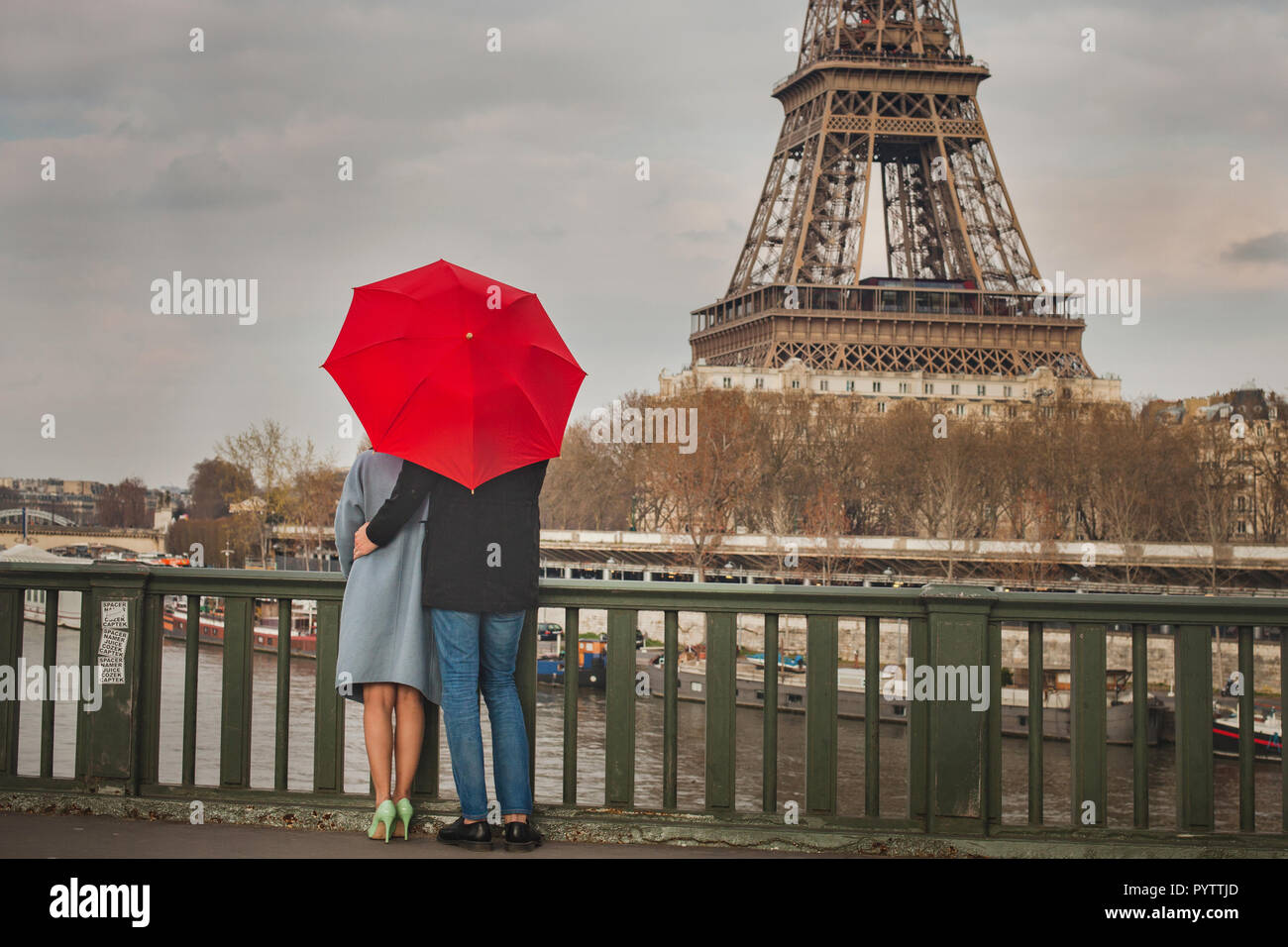 autumn in Paris, couple under red umbrella near Eiffel tower, fall season, love in rainy day, romantic moment on the bridge Stock Photo
