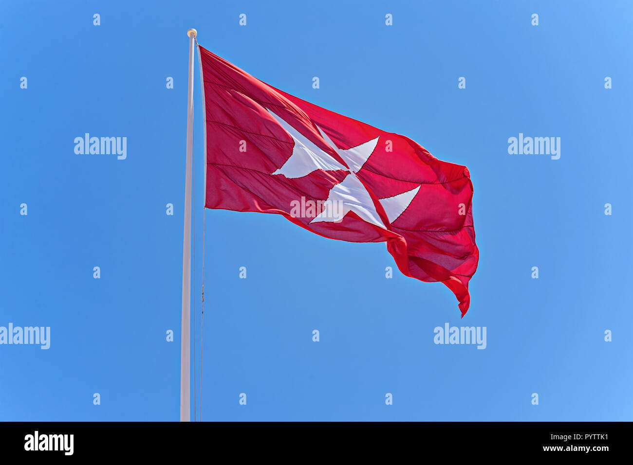 Waving Maltese red flag with a white cross. The symbol of the Knights of Malta is the eight-pointed cross against the blue sky, copy space Stock Photo