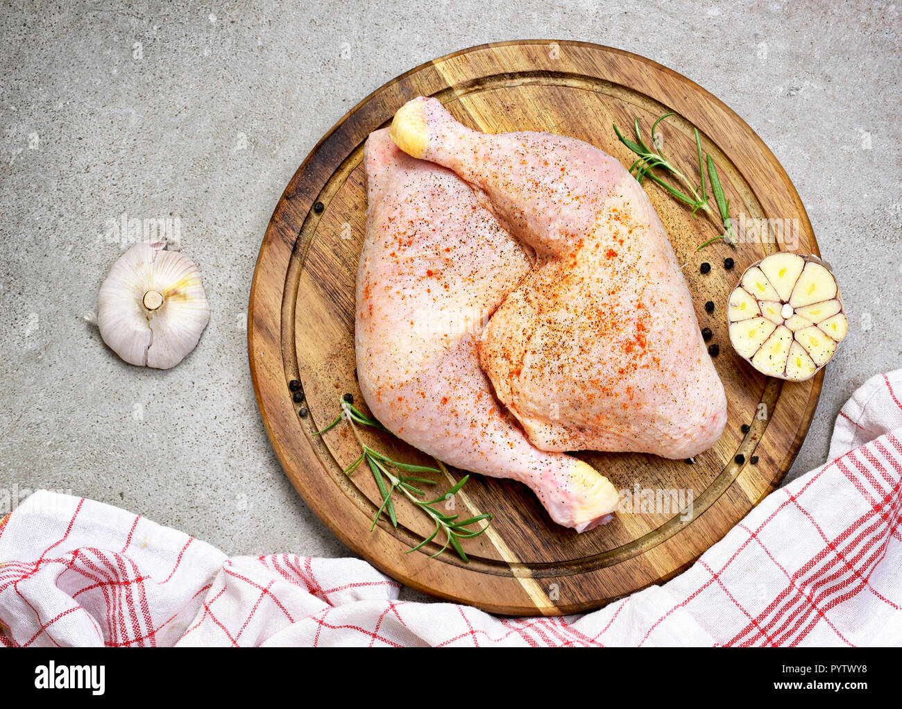 Delicious raw chicken legs or drumsticks on a wooden cutting board. Rustic preparation scene with garlic and raw meat. Stock Photo