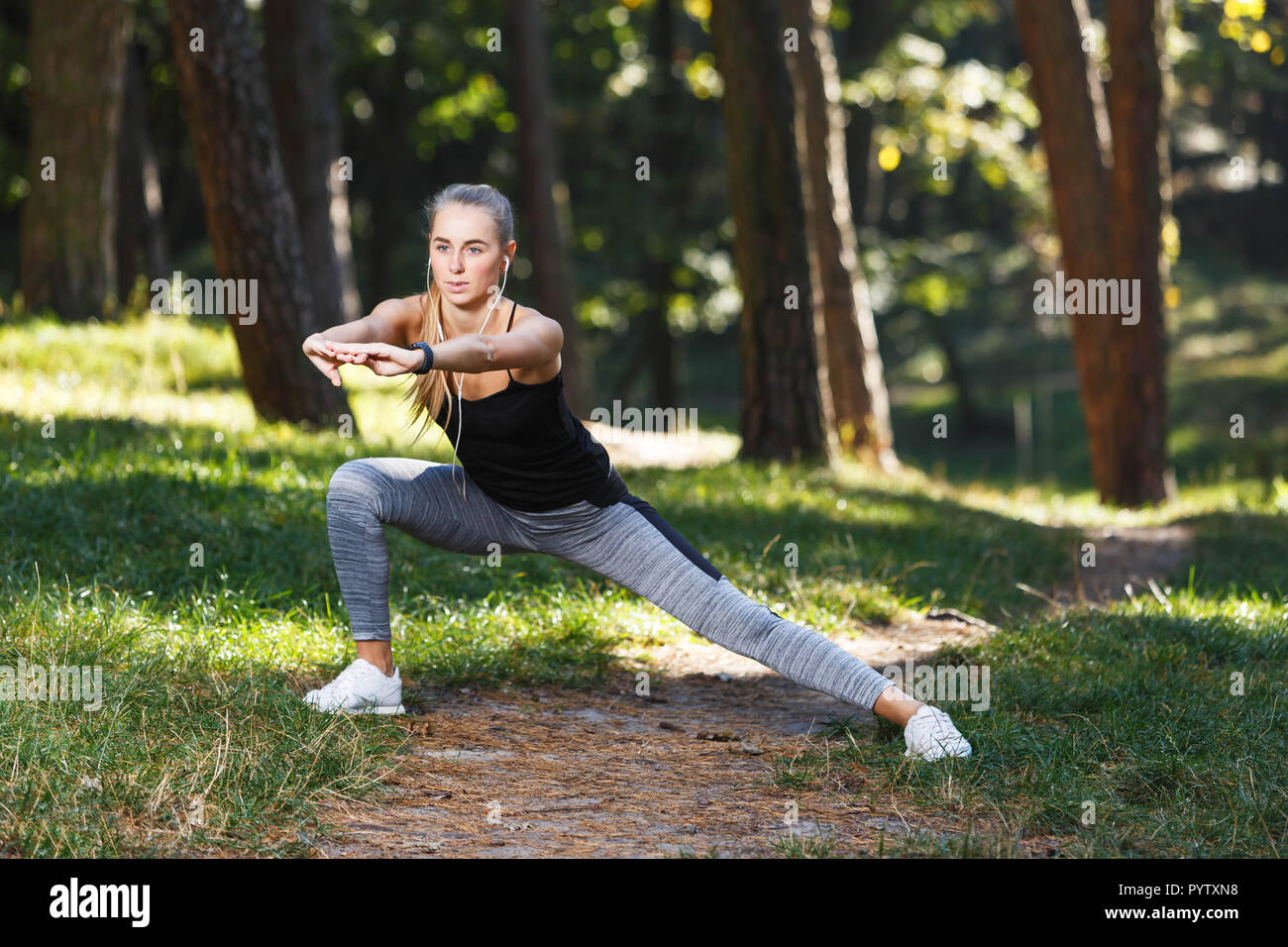 Sportish long-haired young woman wearing black shirt stretching before the running in the sunny park and enjoying of the good weather, healthy lifestyle and people concept Stock Photo