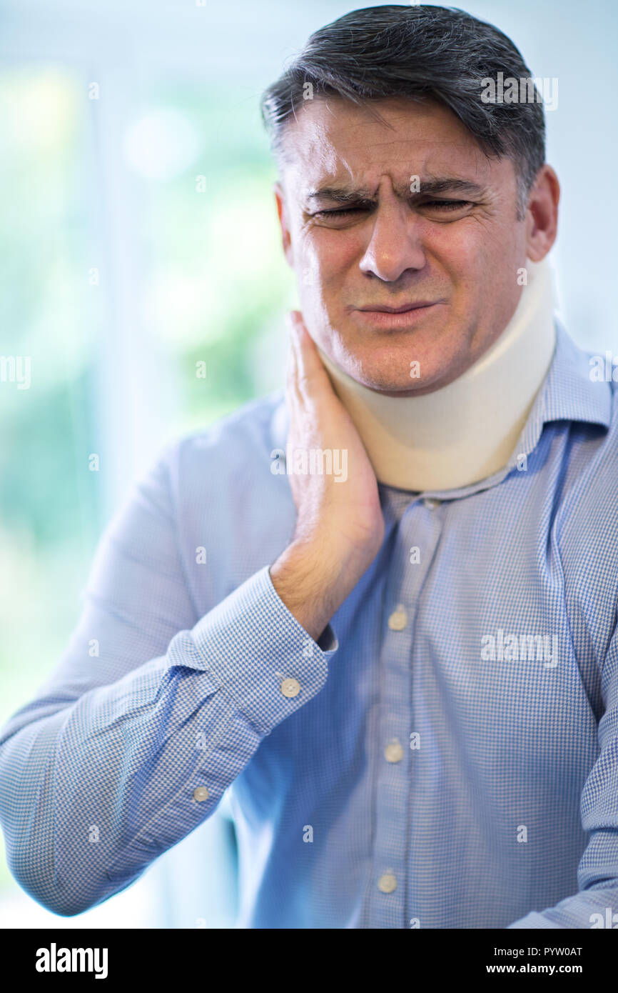 Mature Man Wearing Neck Brace Winces With Pain Stock Photo