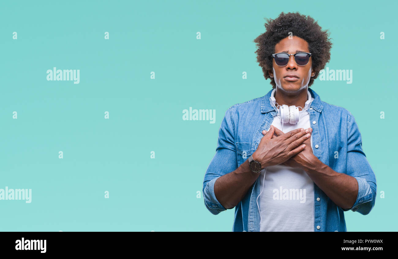 Afro american man wearing headphones listening to music over isolated background smiling with hands on chest with closed eyes and grateful gesture on  Stock Photo