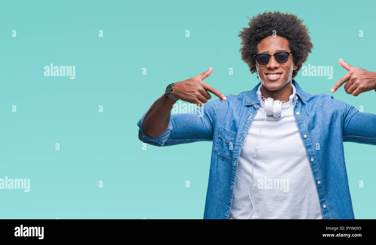 Afro american man wearing headphones listening to music over isolated background looking confident with smile on face, pointing oneself with fingers p Stock Photo