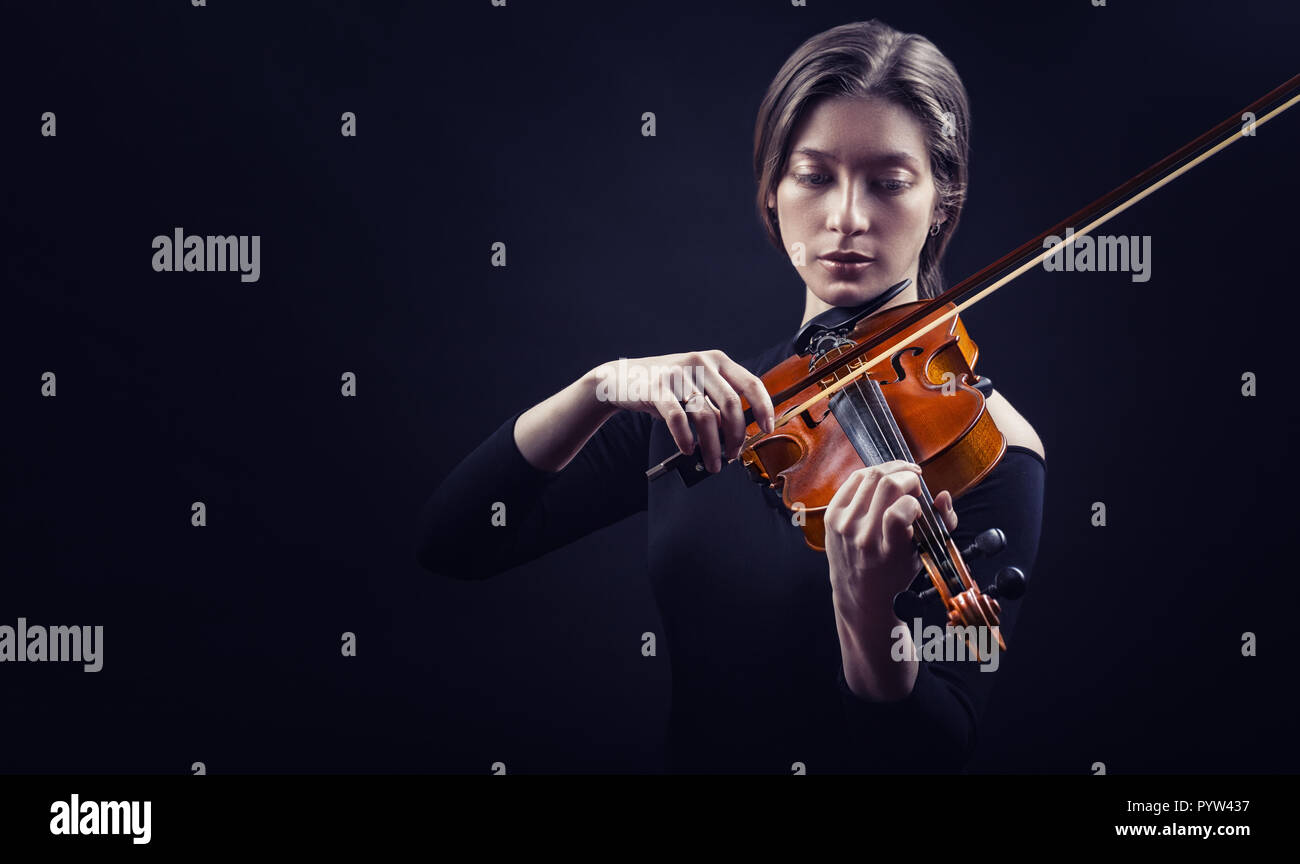 Beautiful young woman playing the violin against a black background Stock Photo